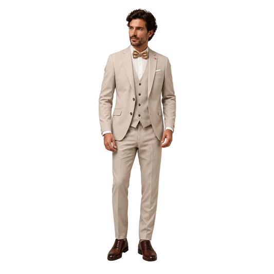 A man standing against a neutral studio backdrop modeling a Digel men's 3-piece ceremony suit in light beige. The formal attire includes a tailored two-button blazer, a matching five-button vest, and slim-fit dress trousers, styled with a white shirt, a gold bow tie, and brown leather oxford dress shoes.