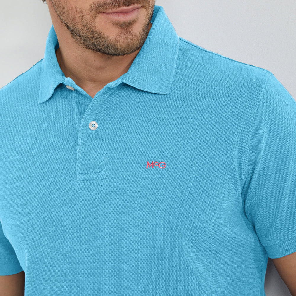 A sea blue colored polo shirt with a collar, buttons, and the McGregor logo embroidered on the chest.
