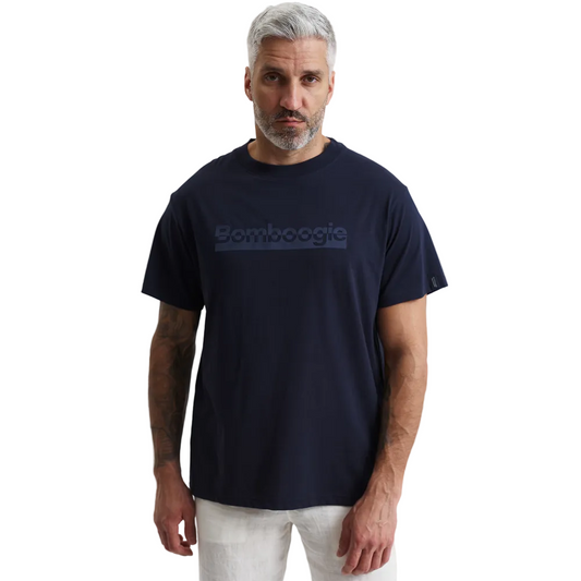 A man modeling a Bomboogie men's navy blue t-shirt against a plain white background. The short-sleeve crewneck shirt features a tonal, rectangular box logo with the text 'Bomboogie' printed across the chest, styled casually with off-white trousers.