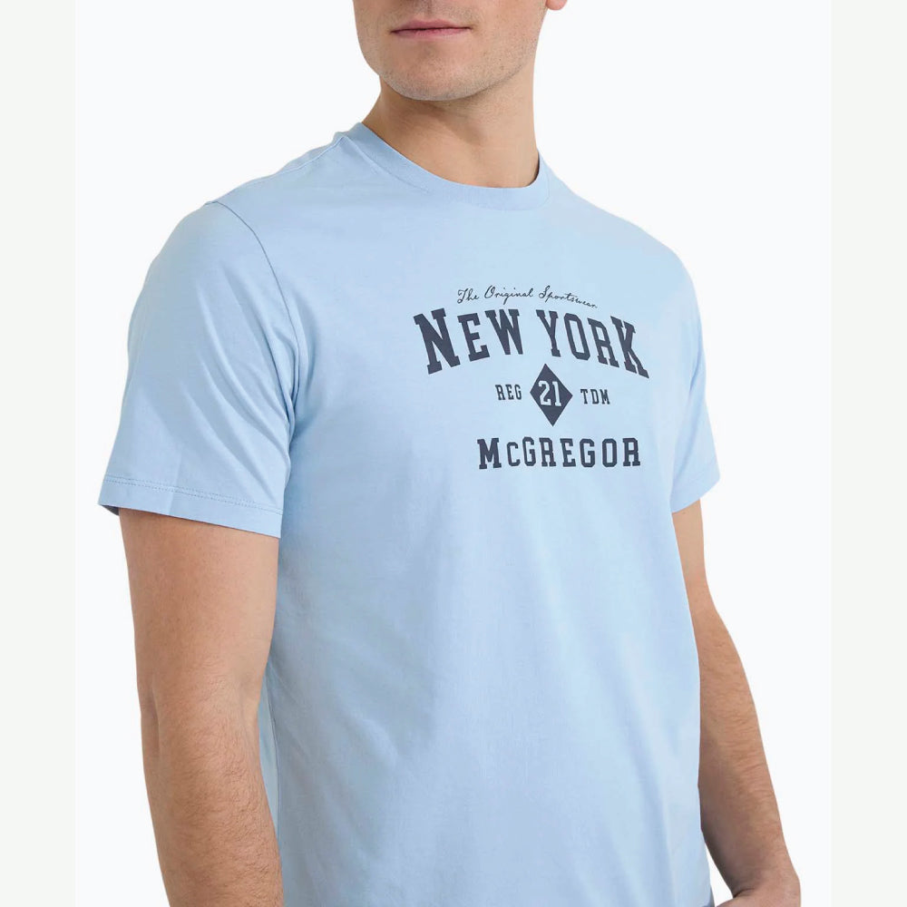 Model wearing a McGregor men's light blue NY graphic crew neck T-shirt with a vintage New York print and short sleeves on a white background.
