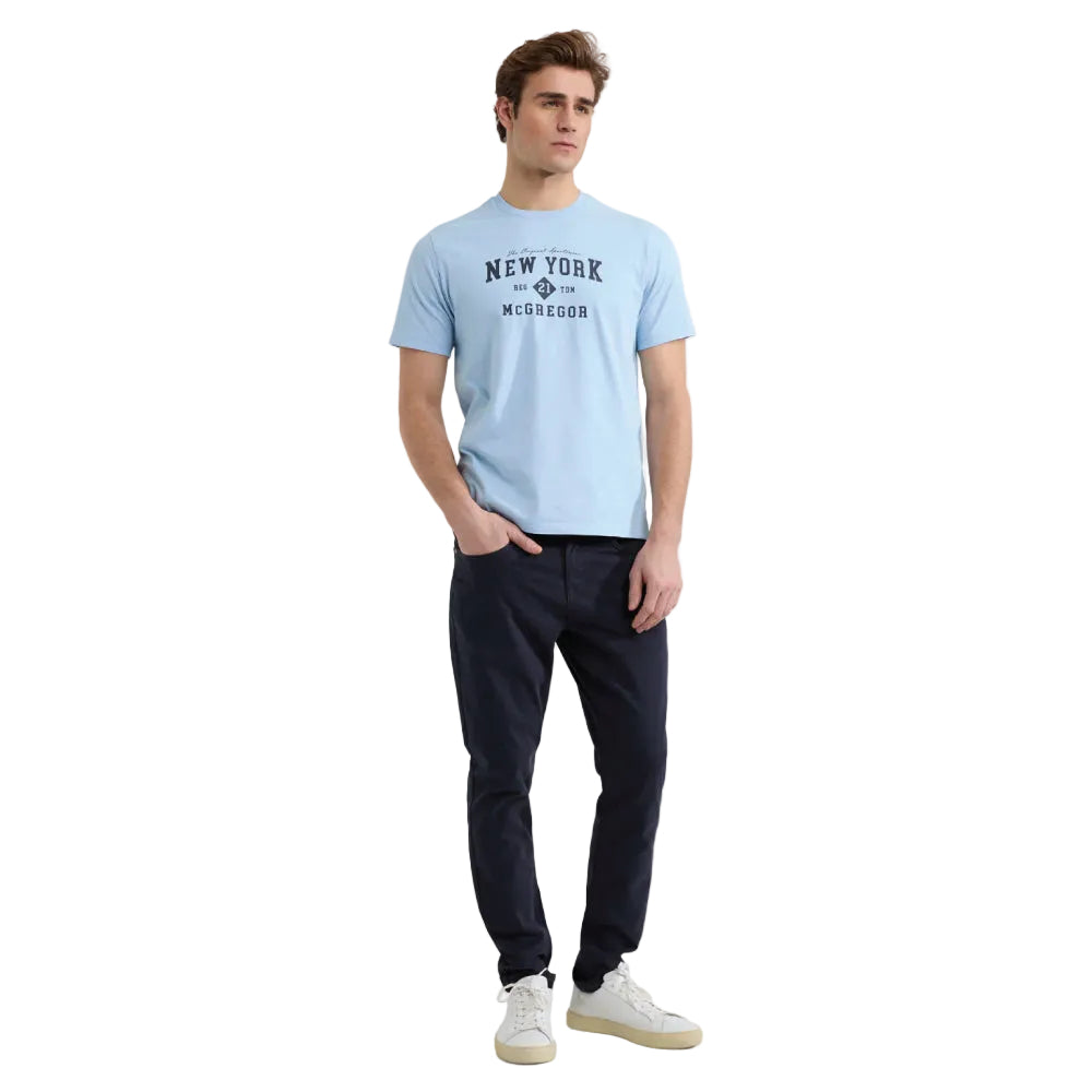 Model wearing a McGregor men's light blue NY graphic crew neck T-shirt with a vintage New York print and short sleeves on a white background.