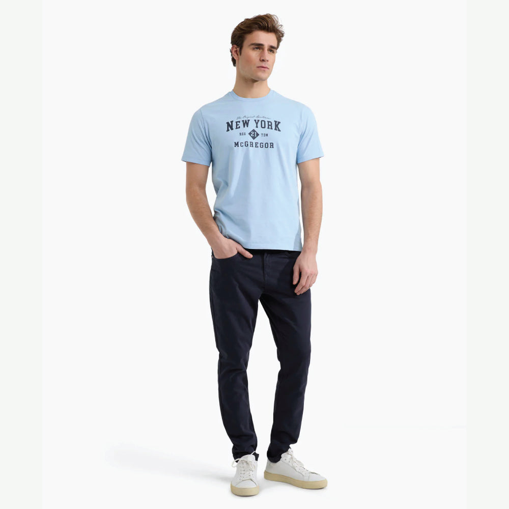 Model wearing a McGregor men's light blue NY graphic crew neck T-shirt with a vintage New York print and short sleeves on a white background.