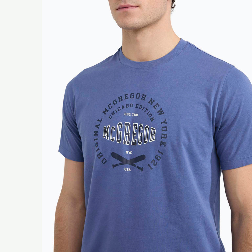 Model wearing a McGregor men's blue Original Print crew neck T-shirt with a vintage logo graphic and short sleeves on a white background.
