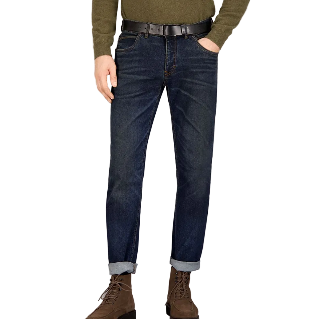 A person standing against a grey background, wearing dark rinse Gardeur jeans with handmade finishings and a rolled-up hem.