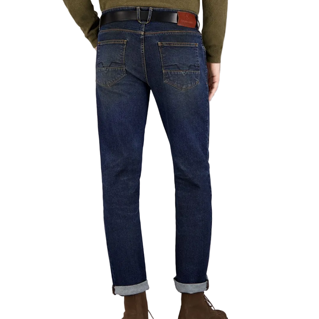 A person standing against a grey background, wearing dark rinse Gardeur jeans with handmade finishings and a rolled-up hem.