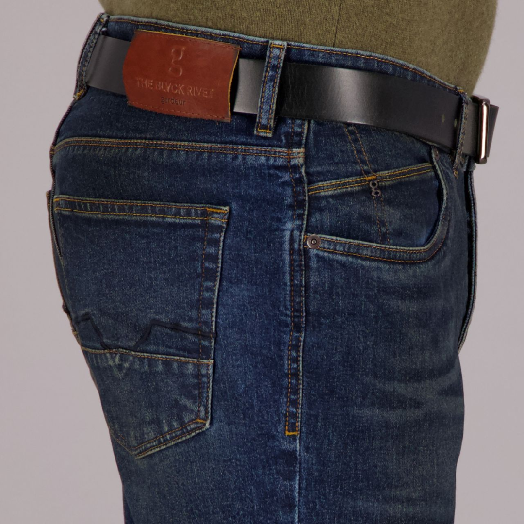 A person standing against a grey background, wearing dark rinse Gardeur jeans with handmade finishings and a rolled-up hem.
