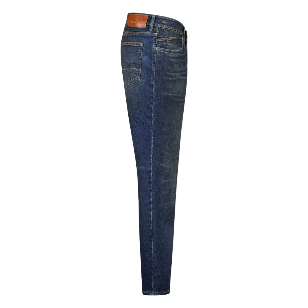 A person standing against a grey background, wearing dark rinse Gardeur jeans with handmade finishings and a rolled-up hem.