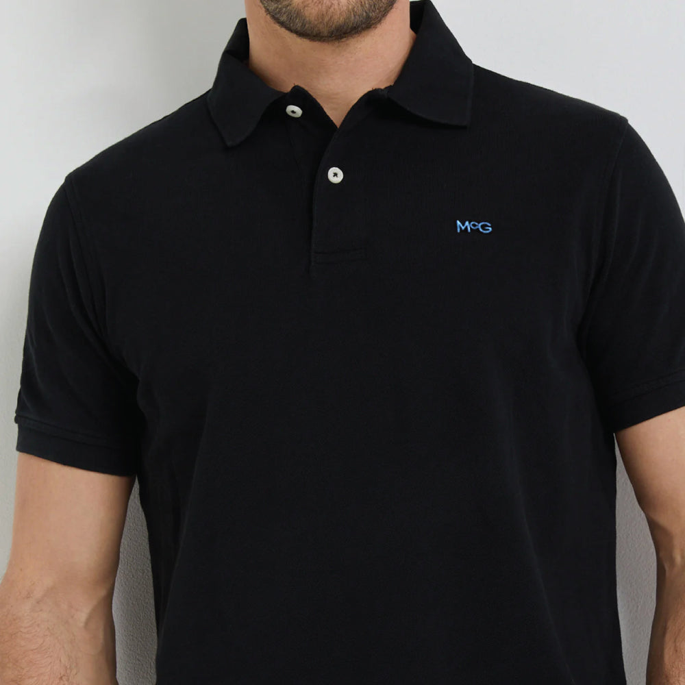 Model wearing a McGregor men's classic regular fit black polo shirt with a ribbed collar and short sleeves on a white background.