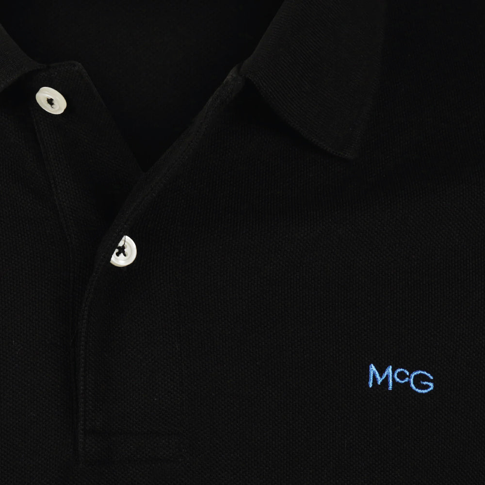 Model wearing a McGregor men's classic regular fit black polo shirt with a ribbed collar and short sleeves on a white background.