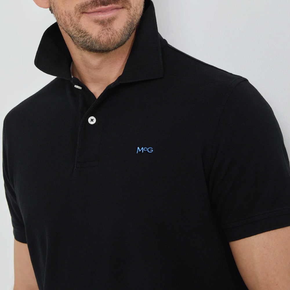 Model wearing a McGregor men's classic regular fit black polo shirt with a ribbed collar and short sleeves on a white background.